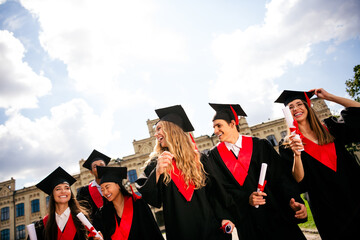 Joyful young graduates celebrating outside in cap and gown on a sunny day at university campus
