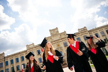Joyful university graduates celebrate with diplomas in hand on a bright summer day, wearing...