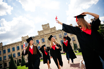 Joyful graduates celebrating on campus, wearing caps and gowns, holding diplomas, having completed...