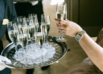 Waiter serves multiple champagne flutes to a guest at a formal event during a daytime gathering