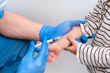 A young male doctor in a blue uniform holds a syringe over a child's arm, vaccinating and donating...