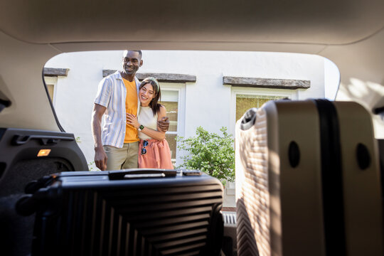 Happy Diverse couple packing suitcases into car trunk, excited for vacation adventure