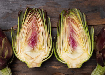 Half and whole purple raw roman artichokes on a dark wooden table top view. Fresh italian vegetables