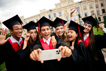 Joyful graduates celebrating on a summer day, capturing memories with a fun selfie outside...
