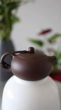 Vertical Screen: A classic dark Yixing clay teapot sits atop a white vessel, with blurred green plants in the background, creating a peaceful and meditative tea-making atmosphere.