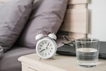 Alarm clock, laptop and glasses on the nightstand. Remote work in the comfort of your own home....