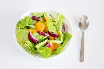 Fresh and healthy salad with mixed vegetables in a white bowl next to a spoon