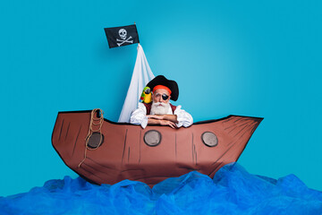 Photo of sad senior man sea robber wearing pirate costume swimming in ship isolated on blue color background