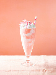 Strawberry milkshake, smoothie, cocktail with whipped cream topping, decorated with edible flowers. Pink background. Copy space.