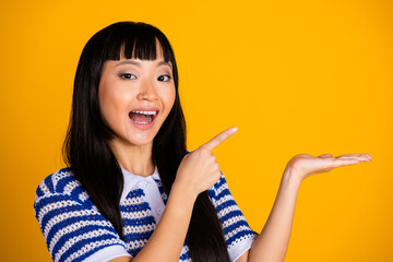 Happy young woman with long black hair gesturing and smiling joyfully against a vibrant yellow...