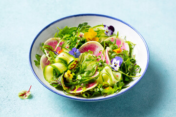 Green salad with watermelon radish and edible flowers in a bowl. Blue background. Close up.