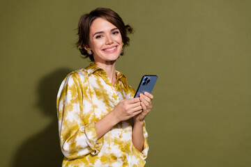 Young brunette woman in a stylish blouse holding a smartphone against a khaki background, exuding a...