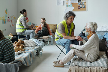 Mature female volunteer in uniform holding hand of senior woman and comforting her while working in...