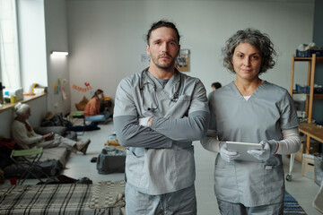 Two confident clinicians or volunteers in medical scrubs looking at camera while standing in...