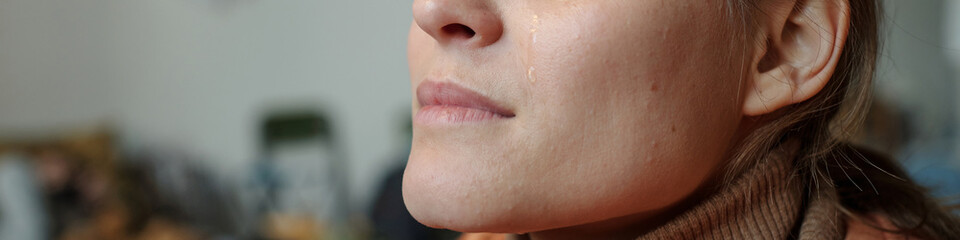 Obraz premium Header of young crying female refugee sitting in front of camera in crisis camp for temporarily homeless people