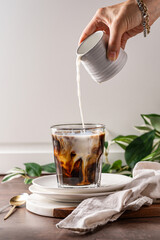milk being poured into a glass of iced coffee, creating delicate swirling patterns. Cold brew iced latte with swirls.