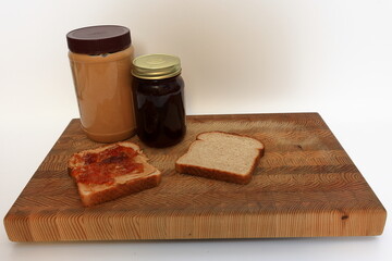 Peanut butter and jelly sandwich, being made on a cutting board before a white background