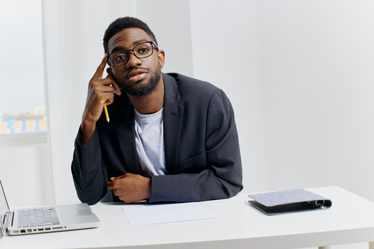 Focused african american man working on laptop at desk with pen in hand, engaged in thoughtful task completion
