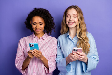 Two smiling young women using smartphones against a purple background, dressed casually, showcasing...
