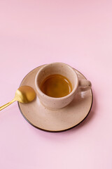 espresso coffee in a beige cup with a gold spoon isolated on the pink background 