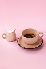 Americano (Lungo) coffee in a beige cup with a milk jug isolated on the pink background