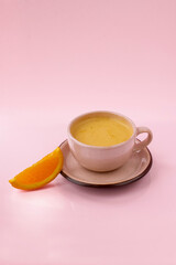 Cappuccino with orange juice with a slice of orange in a beige cup isolated on the pink background
