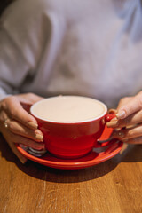 A cozy scene showing hands holding a red cup of a beverage on a wooden surface, highlighting a warm and inviting ambiance.