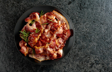 Fried bacon with rosemary on a black stone background.