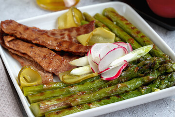 Grilled beef bacon slices with green asparagus on a white ceramic pan