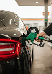 Refueling a black car at a gas station with a green pump nozzle