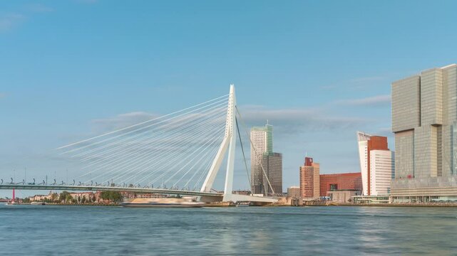 Erasmus Bridge timelapse, called The Swan, spanning the Maas River in Rotterdam, Netherlands. Holland's largest cable-stayed bascule bridge with skyscrapers, boats and a cloudy blue sky backdrop