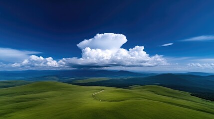 Lush green hills meet a vast, vibrant sky. A large cumulus cloud dominates the upper portion of the image, casting a dramatic contrast against the deep blue expanse.  