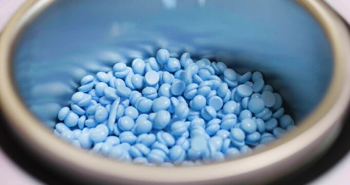 Blue wax beads melting inside professional heater, transforming for precise hair removal treatment, promising silky skin during beauty salon procedure