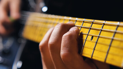 Macro shot of the guitarist's fingers pressing against the bright yellow fretboard. Guitarist...