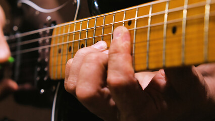 A close-up of a person's hand playing a electric guitar, focusing on the fingers pressing down on the strings and the frets of the guitar neck.