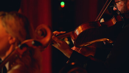 A close-up of a violinist playing an instrument on a dimly lit stage.