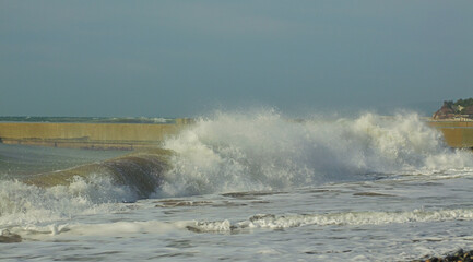 Stormy waves crashing against the coastal barrier. A dynamic view of a stormy sea with large waves crashing against a coastal barrier. The water is a mixture of white foam and dark blue color.