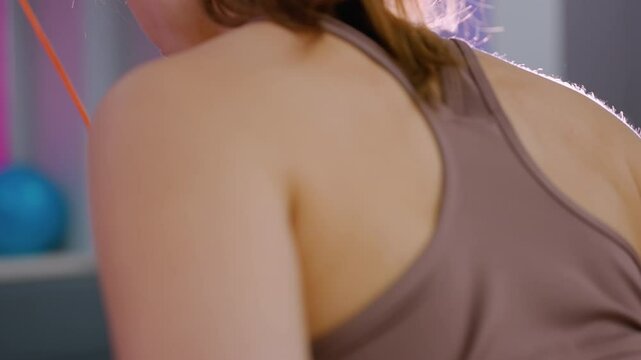Close up side view of young woman slightly bent in brown sportswear pulling weights in gym, focused on strength training with light reflection from right side