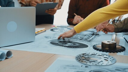 A diverse team collaborates around a table filled with technical drawings and design tools. Focus on hands working on engineering concepts in a modern office setting. SACTR