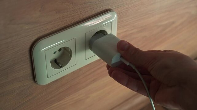 A man uses a socket to plug in an electric cable.
A socket in the wall.
A charger is plugged into a socket.
A charging block