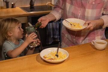 A boy in the kitchen having breakfast holding a bottle of water next to his mother