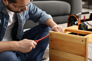 Man repairing wooden stool with screwdriver at home, closeup
