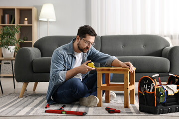 Man using tape measure while repairing wooden stool at home