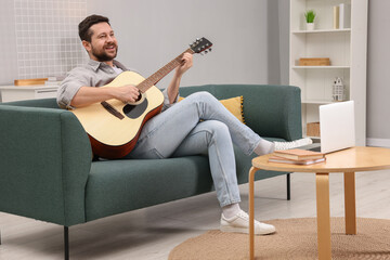 Relaxing hobby. Happy man playing guitar on sofa at home