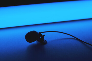 Silhouette of lavalier microphone in blue light on table.