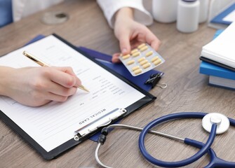 Doctor with pen and blister of pills filling out patient's medical card at wooden table, closeup