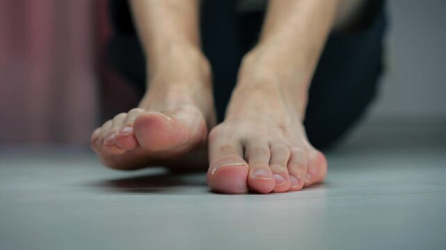 Bare male feet on a wooden floor.
A man sits on the floor.
A man's heels.
A man moves his legs..
Health of feet.