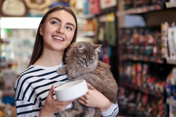 Woman with her cute cat and feeding bowl in pet shop. Space for text © New Africa