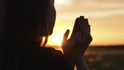 Woman praying with folded hands at sunset silhouette. Religious pious orthodox christian spiritual believing faithful girl at morning dawn sunrise reading prayer bible turning to god jesus christ.