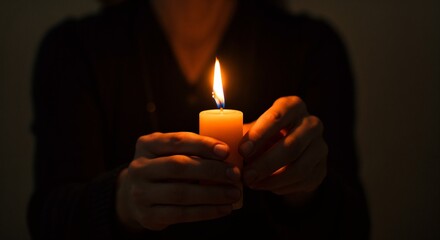 Person holding a lit candle with a flickering flame in a dark setting, conveying warmth and tranquility